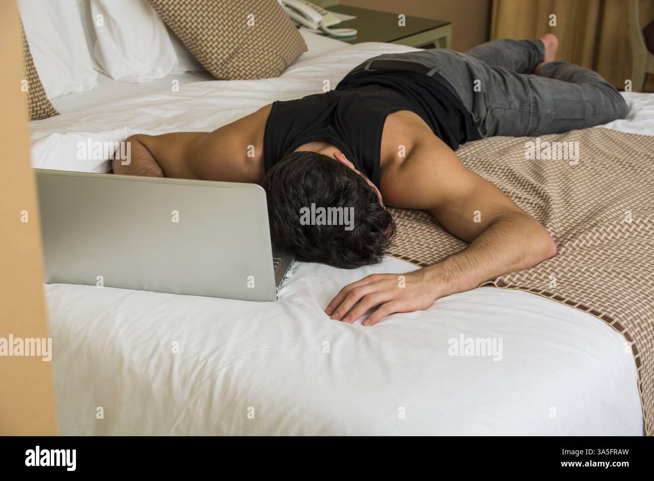 Close Up of assez jeune homme aux cheveux noirs de dormir sur le plancher à côté d'un ordinateur portable avec la main sur le clavier Banque D'Images