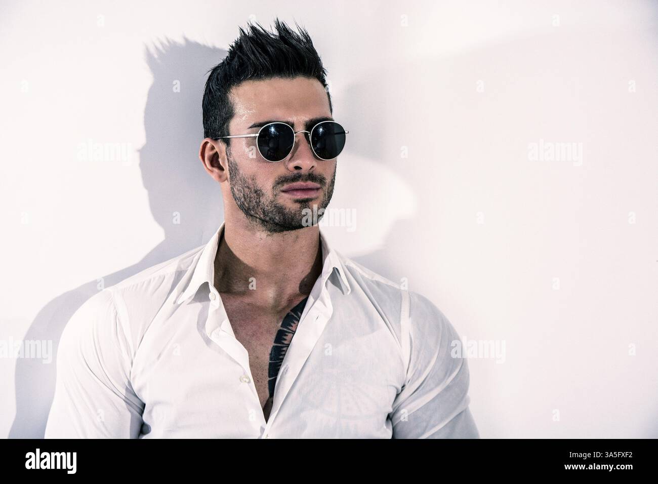 Attrayant élégant jeune homme à la chemise blanche, leaning against wall, looking at camera Banque D'Images