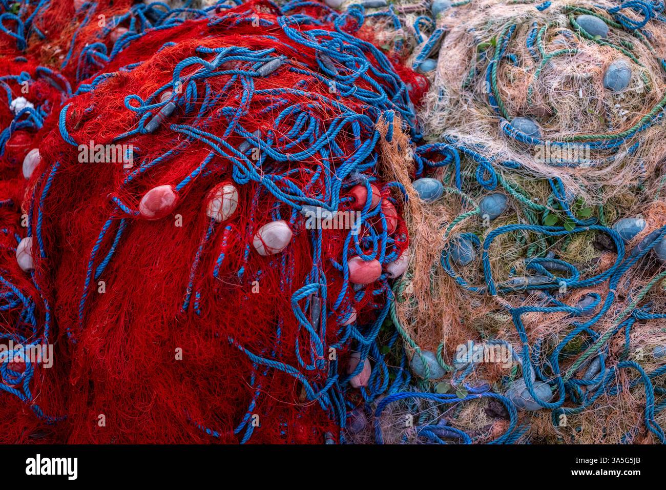 Deux piles de filets de pêche dans des tons rouge vif et beige doux avec des cordes et des flotteurs bleus, montrant contraste et texture. Banque D'Images