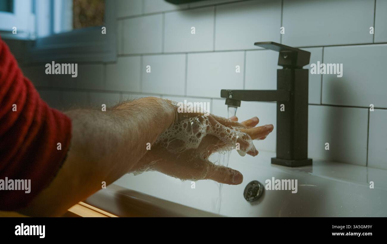 Lavage des mains sous l'eau courante d'un robinet moderne, favorisant l'hygiène, la propreté et les soins personnels dans une salle de bains carrelée Banque D'Images