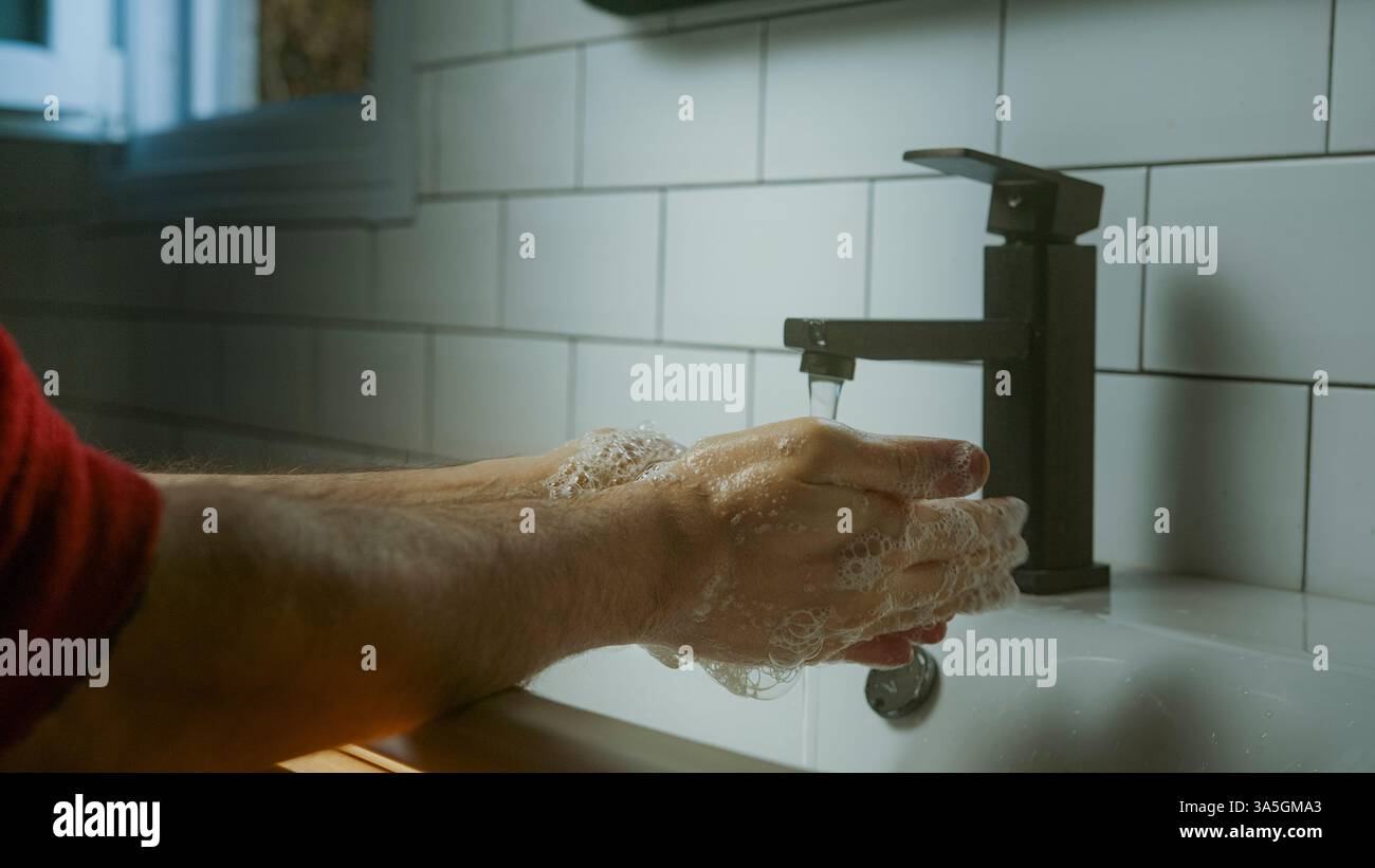 Gros plan de lavage des mains sous l'eau courante d'un robinet moderne, favorisant l'hygiène, la propreté et les soins personnels dans une salle de bains carrelée Banque D'Images