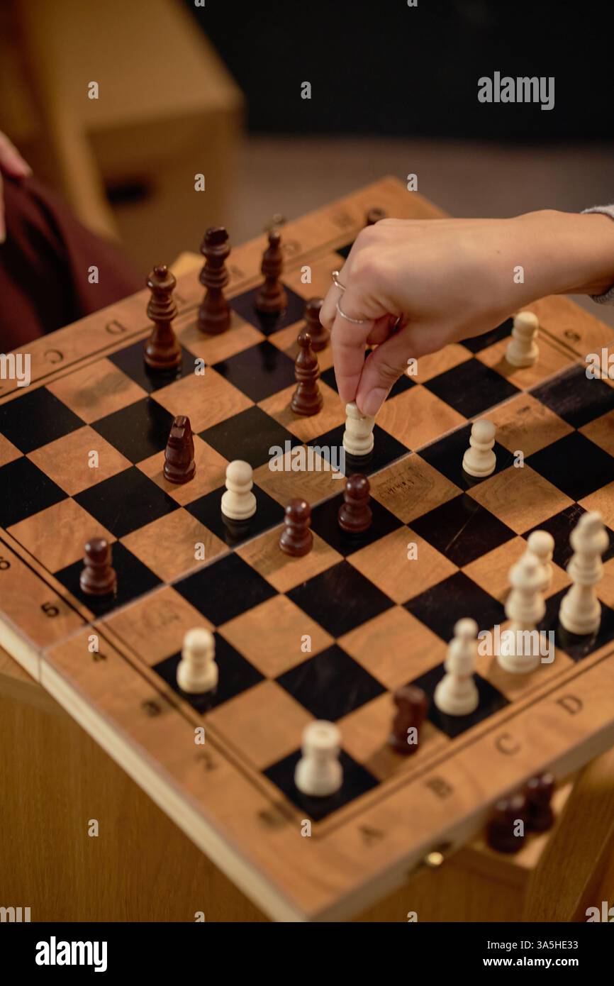Gros plan des mains déplaçant des pièces sur un échiquier en bois pendant un match en intérieur. Les pièces d'échecs dispersées autour du plateau montrent la stratégie de jeu en cours de déroulement Banque D'Images