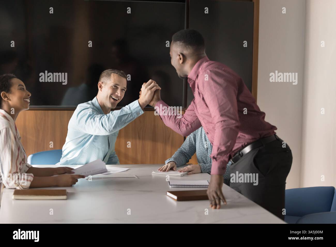 Heureux jeunes coéquipiers multiethniques se saluant, se félicitant ou encourageant avec une poignée de main, un geste d'unité, de respect et d'amitié au workpla Banque D'Images