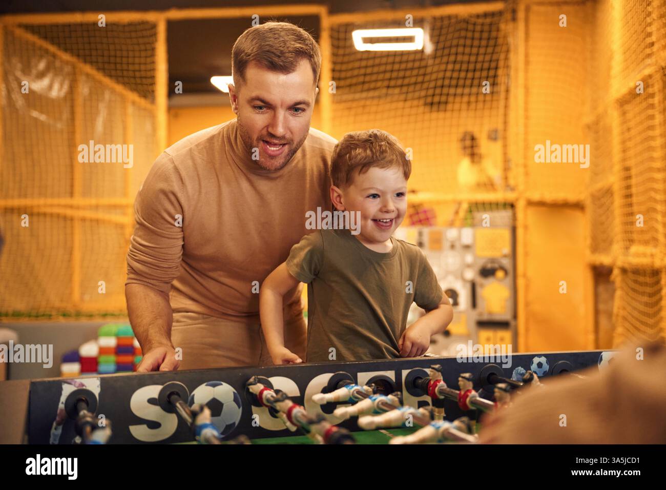 Amuse-toi bien. Famille de papa, mère et fils qui jouent à un jeu de baby-foot à l'intérieur. Banque D'Images