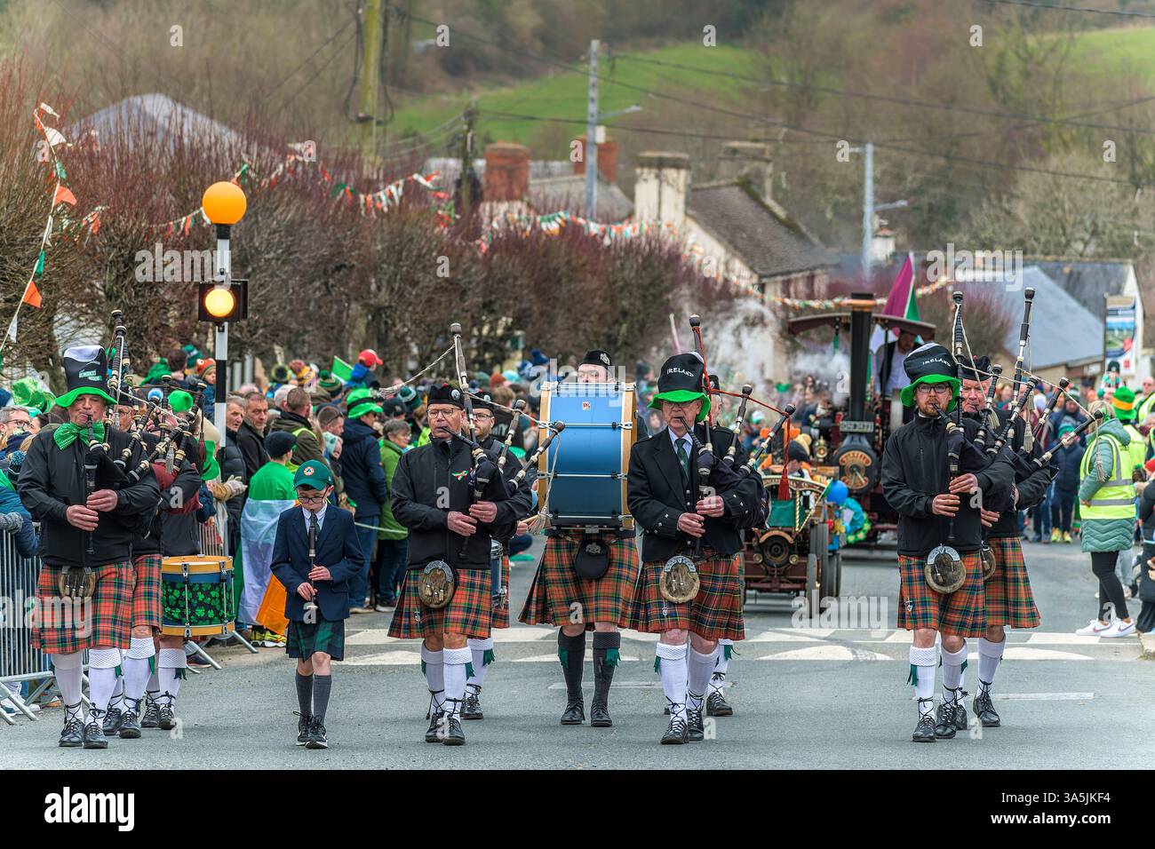 Patrick – Parade. Coolgreany, Irlande. 2025 Irish pipe band marche en kilts et joue de la cornemuse comme une foule dans des acclamations de tenue festive le long des rues Banque D'Images