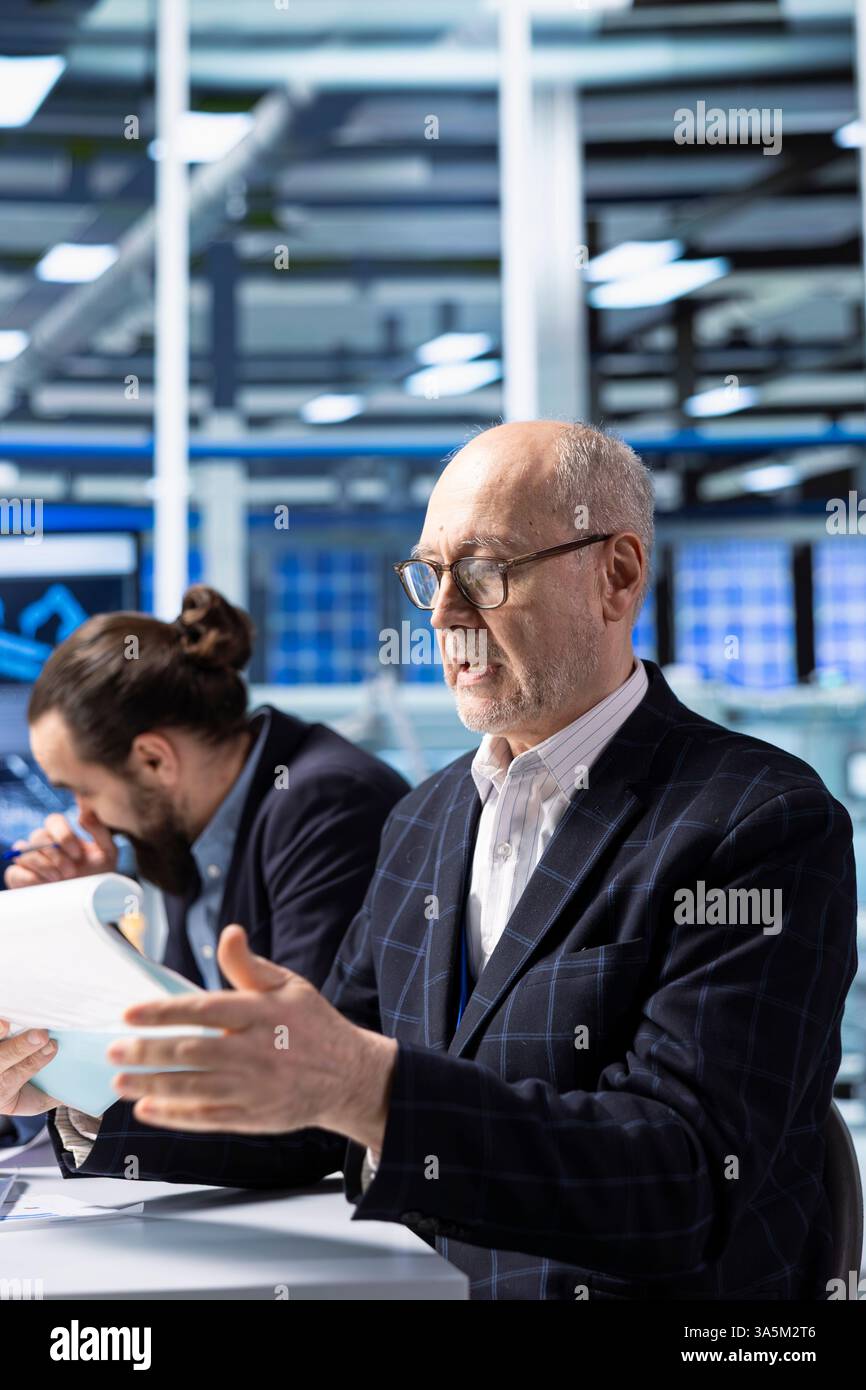 Investisseur senior dans une usine industrielle examinant la documentation avant de conclure l'accord. Vieil homme d'affaires regardant les documents de paperasse pour évaluer la stratégie d'investissement d'affaires dans l'usine industrielle Banque D'Images