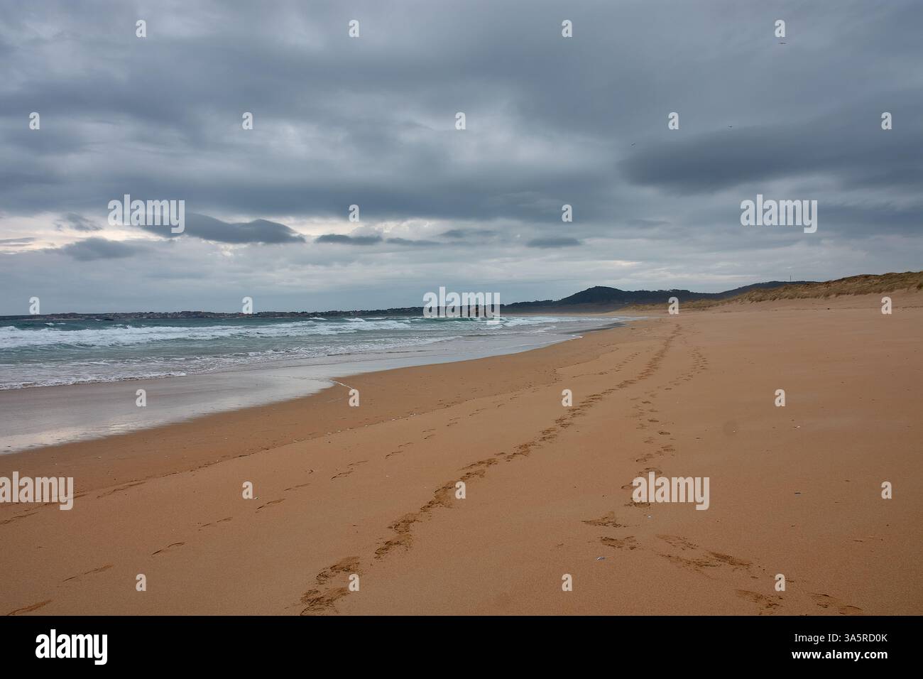 Une plage déserte de Vilar à Corrubedo, Galice, Espagne, par une journée d'hiver avec du sable fin et doux marqué par des empreintes humaines. Le ciel nuageux jette un guichet automatique de mauvaise humeur Banque D'Images