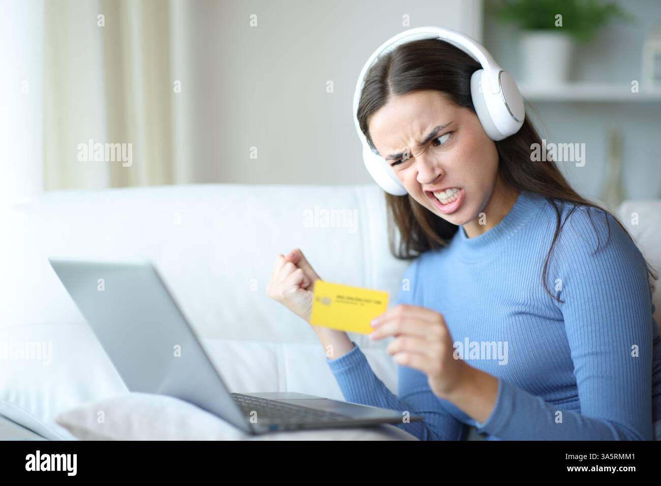 Femme en colère portant casque payant le contenu multimédia en ligne avec carte et ordinateur portable assis sur un canapé à la maison Banque D'Images