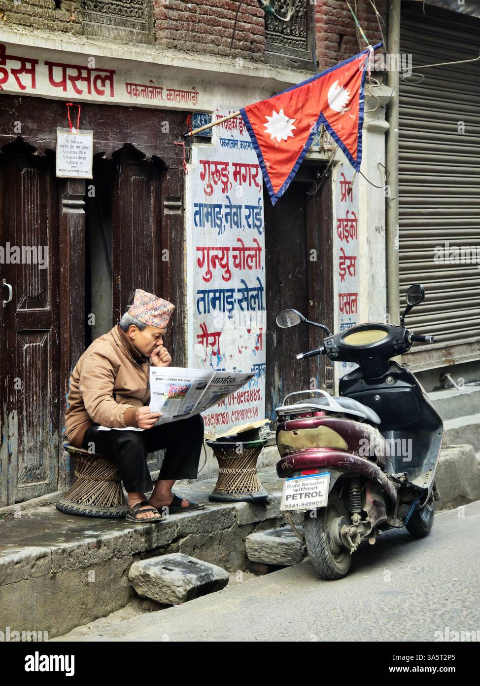 Un homme népalais lisant le journal du matin près d'une vieille maison dans le quartier de Thamel à Katmandou, au Népal. Banque D'Images