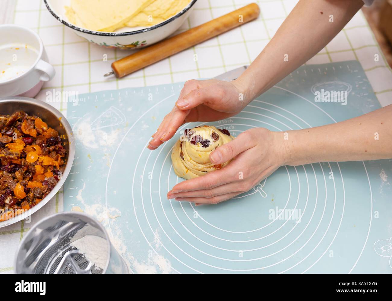 Les mains d'une jeune femme caucasienne façonnent soigneusement un pain de Pâques sucré, rempli de fruits secs. La pâtisserie festive est presque prête pour la cuisson. Banque D'Images