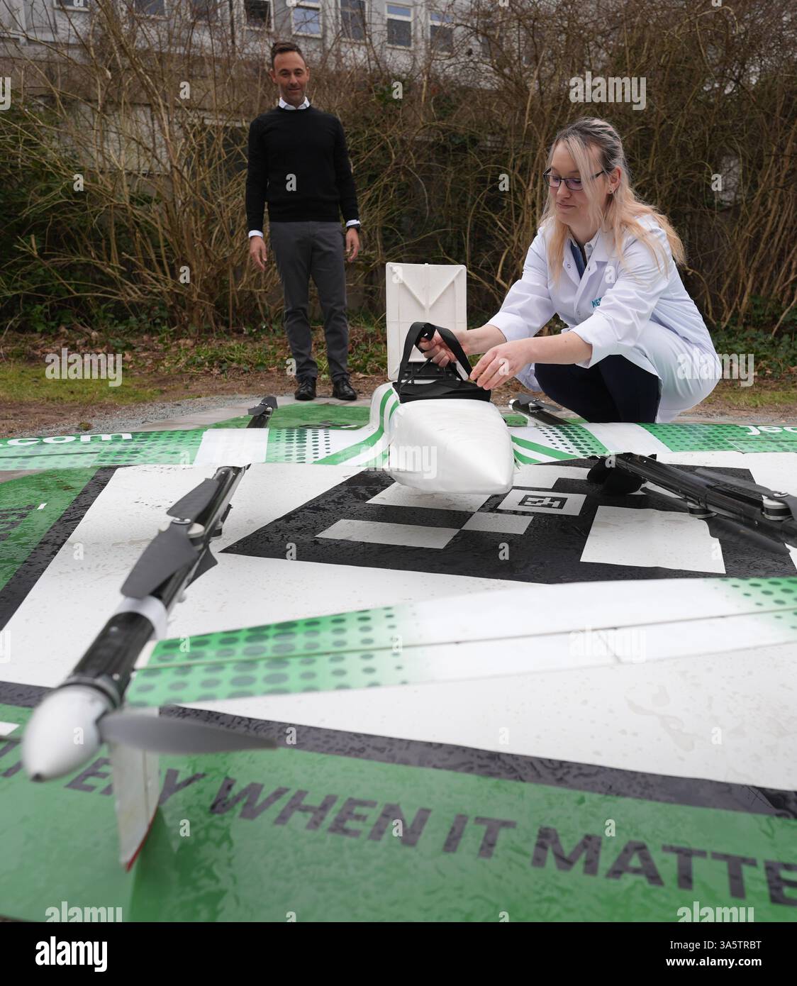 24 mars 2025, Schleswig-Holstein, Bad Oldesloe : Susann Miller, responsable de laboratoire sur le site de Bad Oldesloe Medical technologies for Laboratory Analytics (MTL), retire un sac d'échantillons du drone de transport Jedsy après le premier vol de ligne de drone pour des échantillons de laboratoire sur le terrain d'Asklepios Klinik Bad Oldesloe. Daniel Amrein, directeur général d'Asklepios Kliniken Hamburg GmbH, se trouve à gauche sur la photo. En fonctionnement régulier, le drone transporte des échantillons de laboratoire de la clinique privée Asklepios Blomenburg à Selent à la clinique Asklepios à Bad Oldesloe, à environ 60 kilomètres Banque D'Images