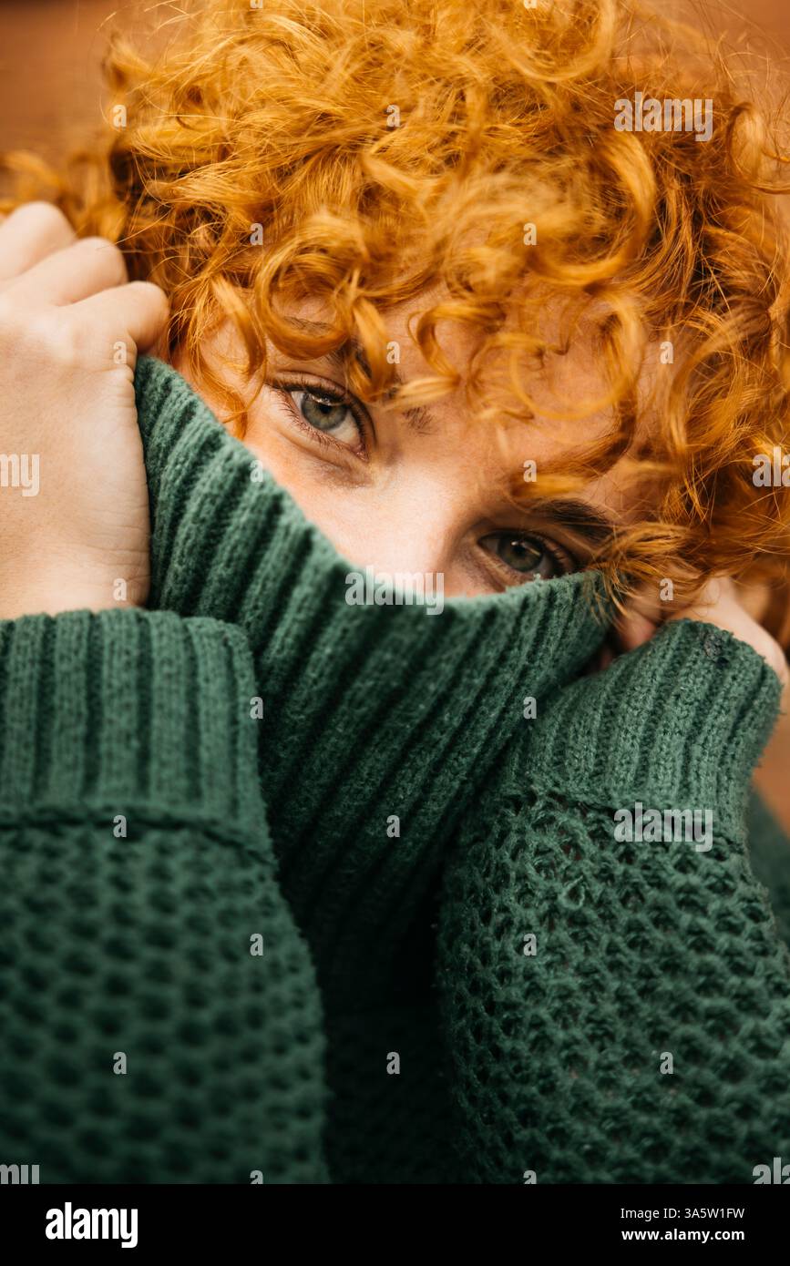Femme avec des cheveux bouclés de gingembre couvrant son visage avec un pull en laine verte Banque D'Images Femme avec des cheveux bouclés de gingembre couvrant son visage avec un pull en laine verte Banque D'Images