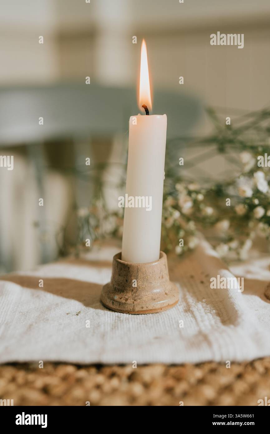 Une bougie est allumée sur une table avec un tissu blanc. La bougie est entourée de fleurs, ce qui ajoute une touche d'élégance et de chaleur à la scène. Concept de Banque D'Images
