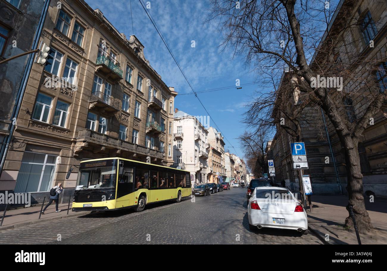 Lviv, Ukraine - 22 mars 2025 : un bus jaune coloré navigue dans les charmantes rues pavées de Lviv, entourées de bâtiments historiques et d'une Sere Banque D'Images