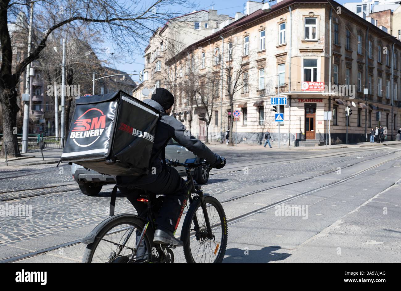 Lviv, Ukraine - 22 mars 2025 : un cycliste traverse les rues animées de Lviv, Ukraine, livrant de la nourriture par une journée ensoleillée tout en naviguant dans l'agitation Banque D'Images
