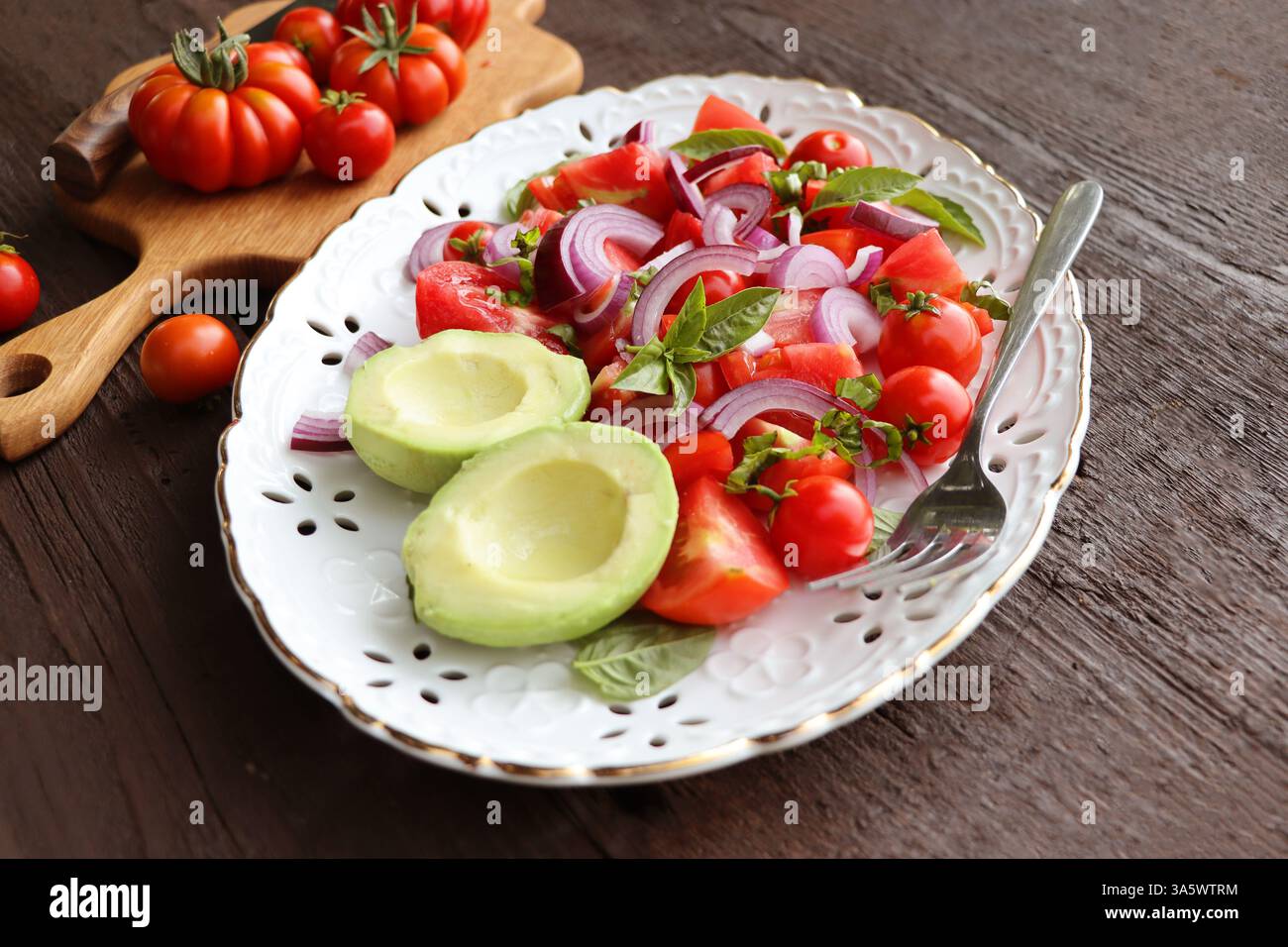 Salade d'avocat et de tomates fraîches et saines avec des oignons sur fond rustique foncé. Banque D'Images
