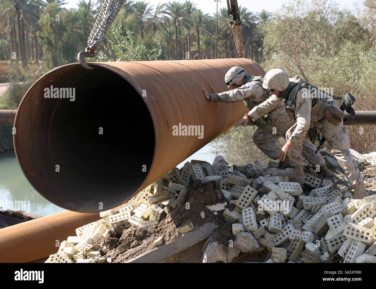 13 novembre 2004 ; Lutafiyah, IRAK ; Un marin et un marin affectés à la 24e unité expéditionnaire des Marines (24e MEU) guident un tuyau dans une rivière à Lutafiyah, Irak. Les tuyaux ont servi de base à un pont reconstruit qui a été gravement endommagé lors d'attaques répétées de militants anti-irakiens. La 24e MEU mène actuellement des opérations de sécurité et de stabilité dans la province de Babil du Nord. Banque D'Images
