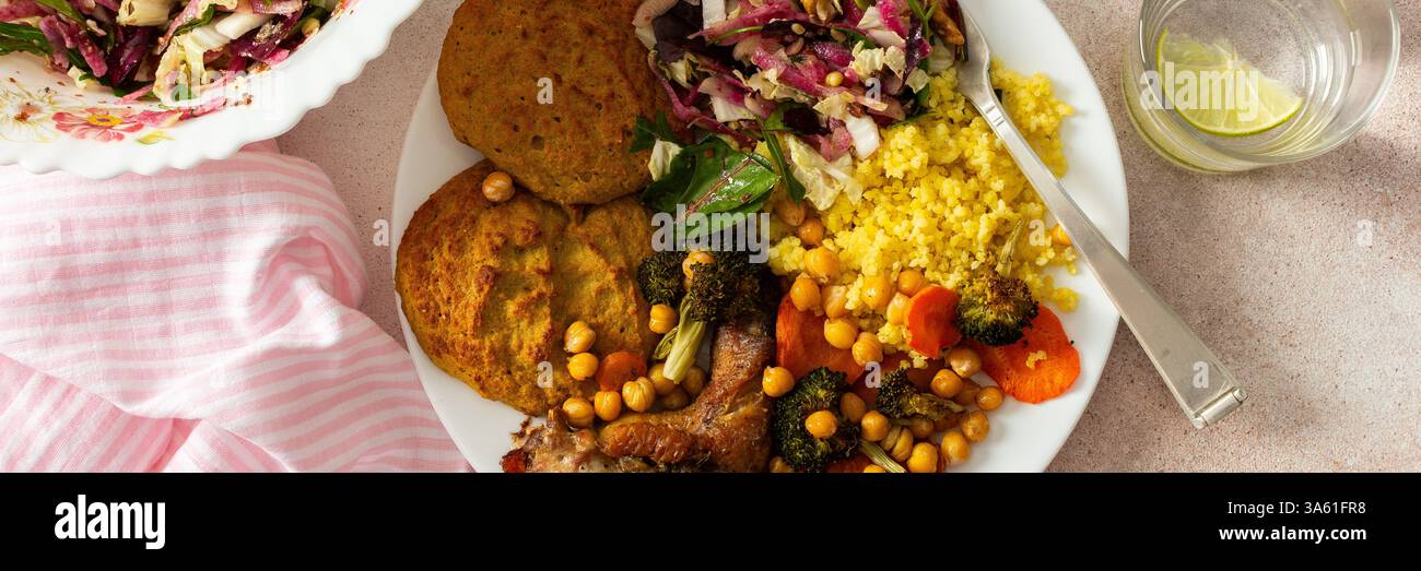 Un petit déjeuner nutritif et copieux composé de crêpes aux courgettes aux lentilles, millet, cou de poulet cuit au four, patates douces rôties, brocoli, carottes, pois chiches, avec un f Banque D'Images