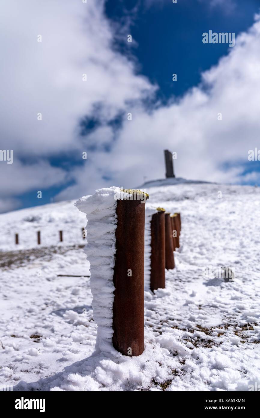 Bâtons rouillés couverts de neige et de glace sur une montagne enneigée avec un monument au sommet, sous un ciel bleu nuageux Banque D'Images