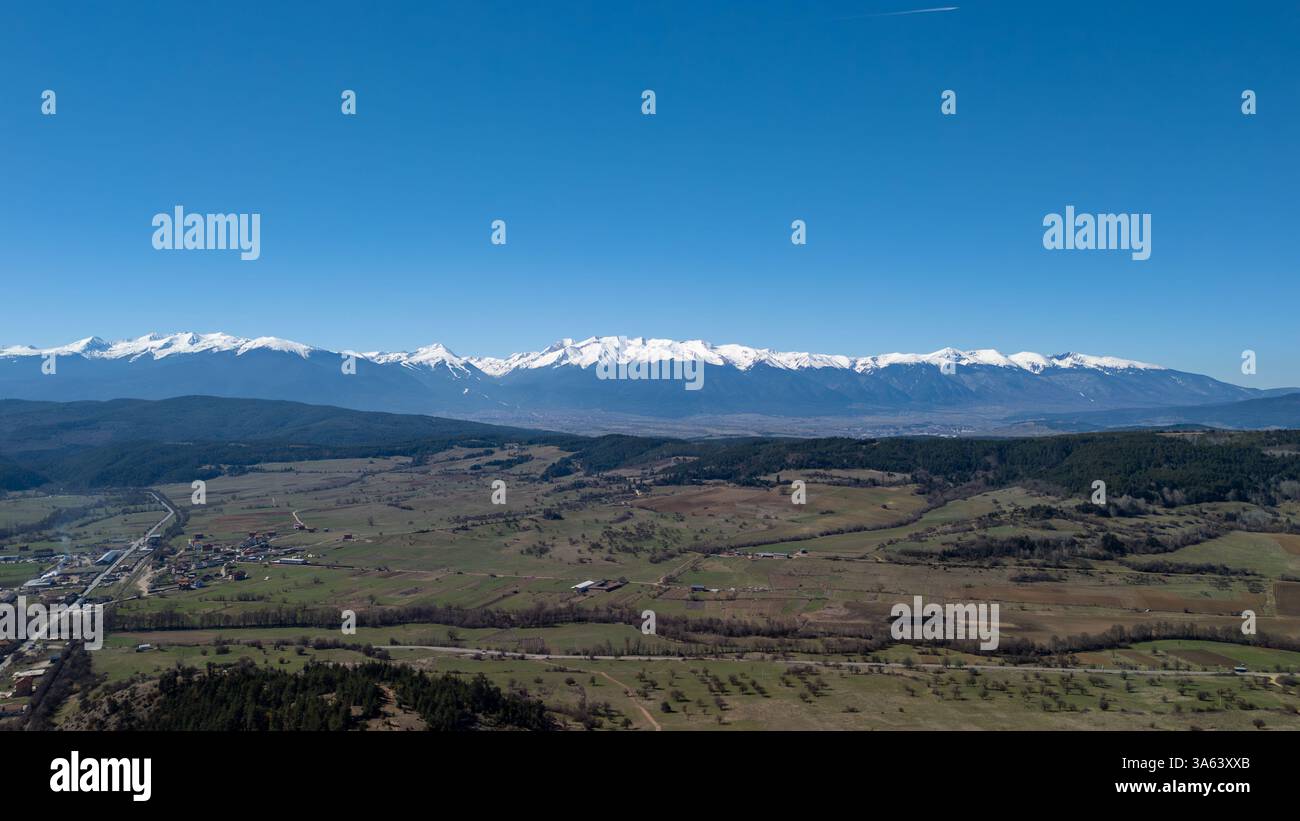 Superbe vue aérienne de la montagne Rila enneigée surplombant une vallée pittoresque en Bulgarie, baignée par la lumière chaude du soleil d'une journée de printemps claire Banque D'Images