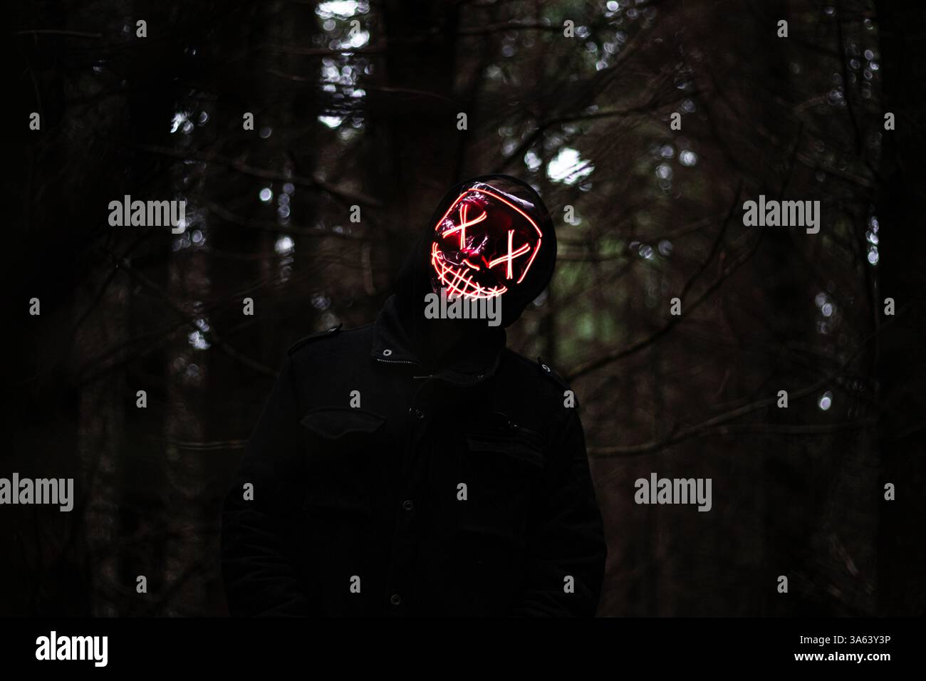 Figure terrifiante de masque de lapin LED se cachant dans la forêt sombre - Halloween Nightmare Banque D'Images