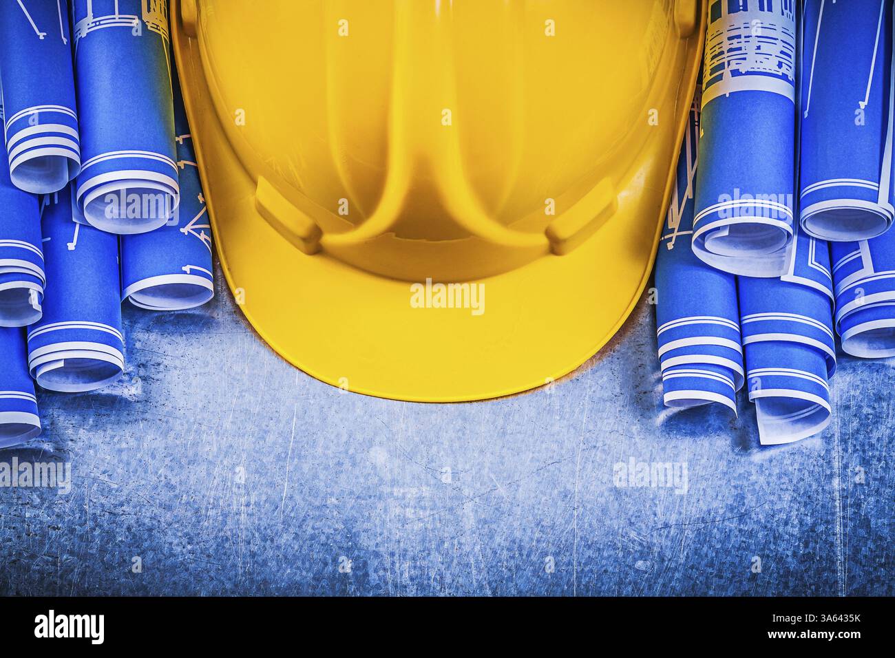 Casque de construction jaune de dessins d'ingénierie roulés bleus sur le concept de construction de fond métallique Banque D'Images
