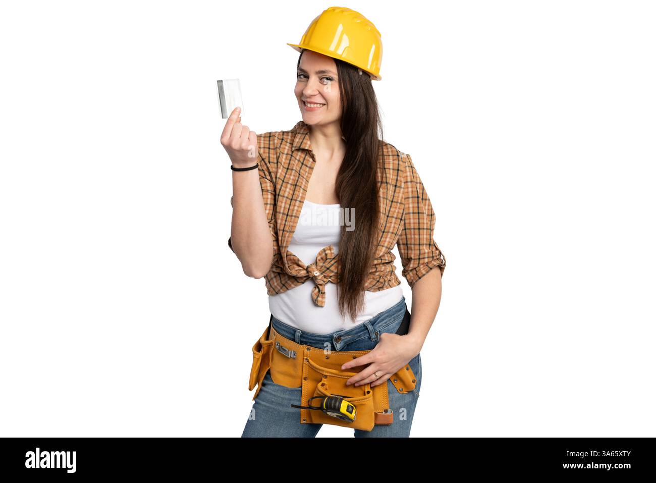 Une femme joyeuse ouvrière de la construction dans un casque de sécurité et une ceinture à outils, affichant avec confiance une carte de crédit, symbolisant l'autonomisation financière et la sécurité Banque D'Images