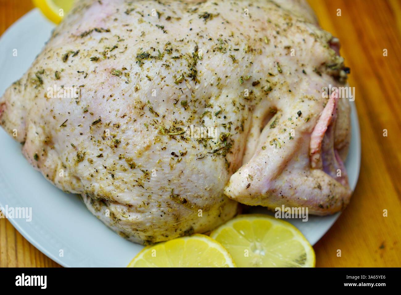 Poulet entier cru enrobé d'herbes aromatiques provençales et d'assaisonnements, placé sur une assiette blanche avec des tranches de citron frais sur une table en bois rustique. Le poulet est préparé pour la torréfaction, mettant l'accent sur la cuisine maison et la préparation des repas gastronomiques. Banque D'Images Poulet entier cru enrobé d'herbes aromatiques provençales et d'assaisonnements, placé sur une assiette blanche avec des tranches de citron frais sur une table en bois rustique. Le poulet est préparé pour la torréfaction, mettant l'accent sur la cuisine maison et la préparation des repas gastronomiques. Banque D'Images