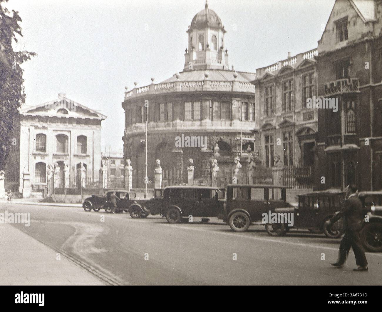 Oxford, Oxfordshire, Angleterre : architecture historique de l'Université d'Oxford. Le bâtiment en forme de dôme est la Radcliffe Camera, l'un des monuments les plus emblématiques d'Oxford. Autour de lui se trouvent des parties de la Bodleian Library, une pièce maîtresse du patrimoine académique d'Oxford. Sur la route à côté de ces bâtiments se trouve une rangée de voitures à moteur. D'après un album de photographies non datées des années 1920, principalement de la mode britannique et de l'histoire sociale. Les photos originales étaient principalement d'environ 3x2 pouces, ton sépia, et prises par un bon photographe amateur. Banque D'Images