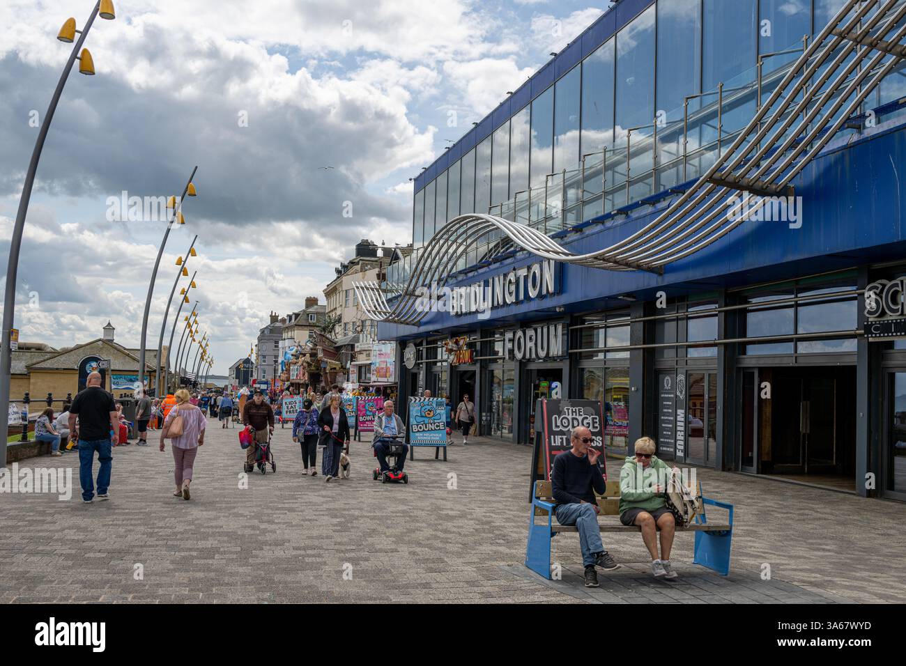 Les touristes se promènent le long de l'Esplanade de Bridlington, en passant par l'extérieur moderne du complexe Forum. Yorkshire de l'est. ROYAUME-UNI Banque D'Images