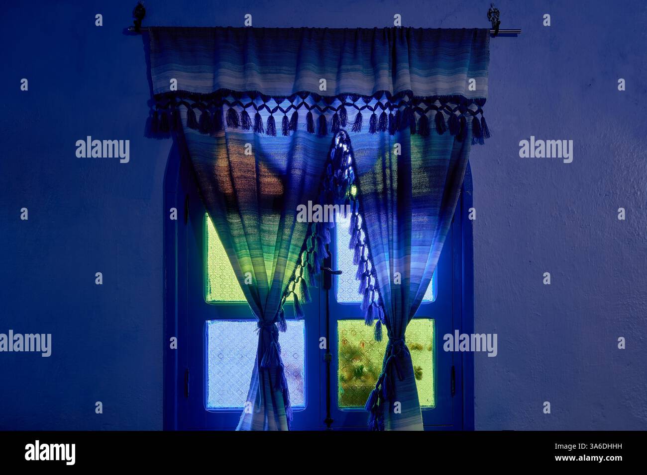 Lumière naturelle diffusée à travers des rideaux encadrés de vitraux en verre vert, bleu et jaune dans une fenêtre en bois voûtée fermée, Chefchaouen, Maroc Banque D'Images