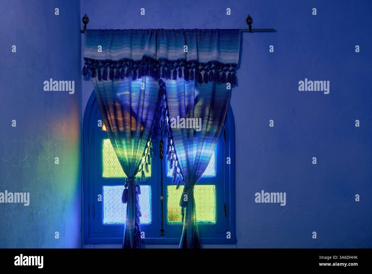 Couleurs diffusées lumière venant à travers des rideaux encadrés de vitraux en verre vert, bleu et jaune dans une fenêtre en bois voûtée fermée, Chefchaouen, Maroc Banque D'Images