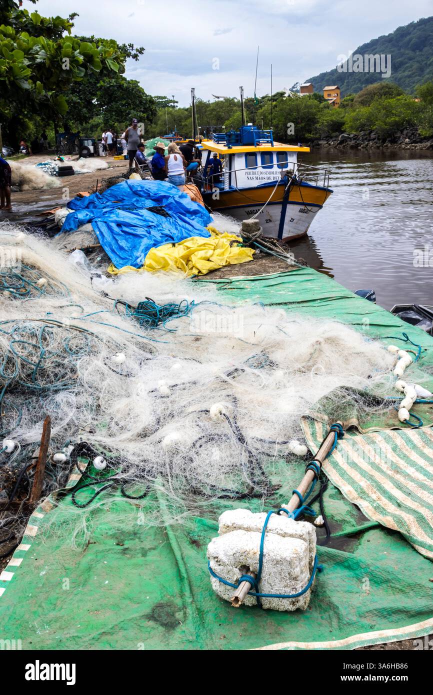 Peruibe, Sao Paulo, 17 janvier 2025. Scène de port de pêche à Peruíbe, état de Sao Paulo. Les filets colorés, les bateaux et la toile de fond de la forêt atlantique capturent t Banque D'Images
