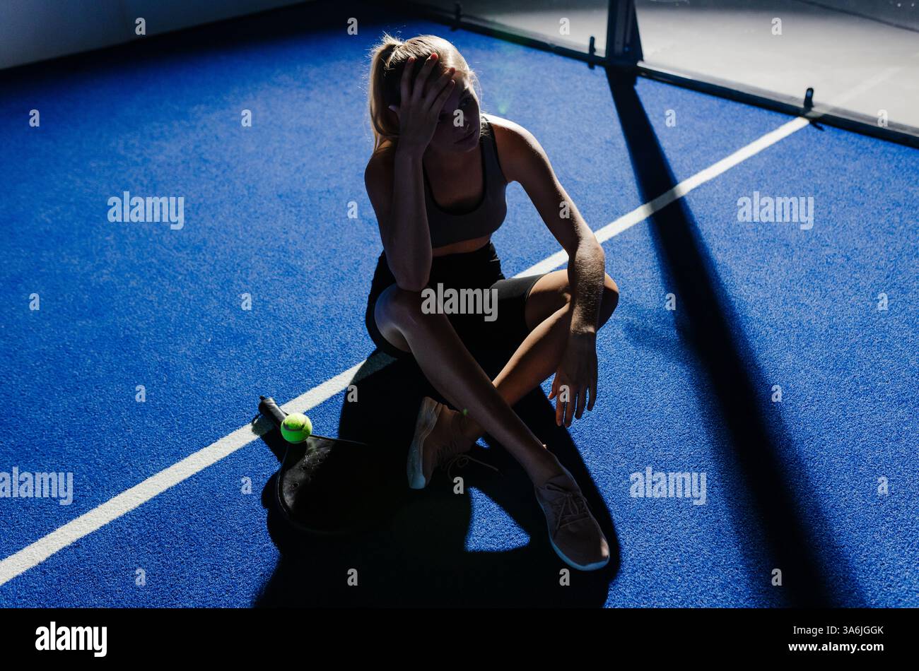 Athlète féminine épuisée assise sur un court de padel, se tenant la tête dans la frustration Banque D'Images
