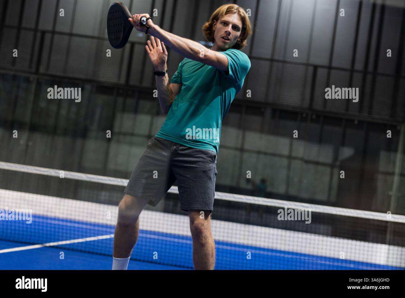 Jeune homme jouant au padel, raquette oscillante avec concentration et détermination Banque D'Images