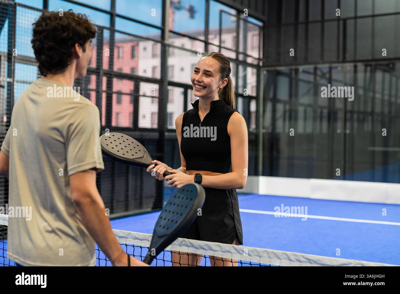 Jeune femme et homme jouant au padel, souriant et tenant des raquettes sur le court Banque D'Images