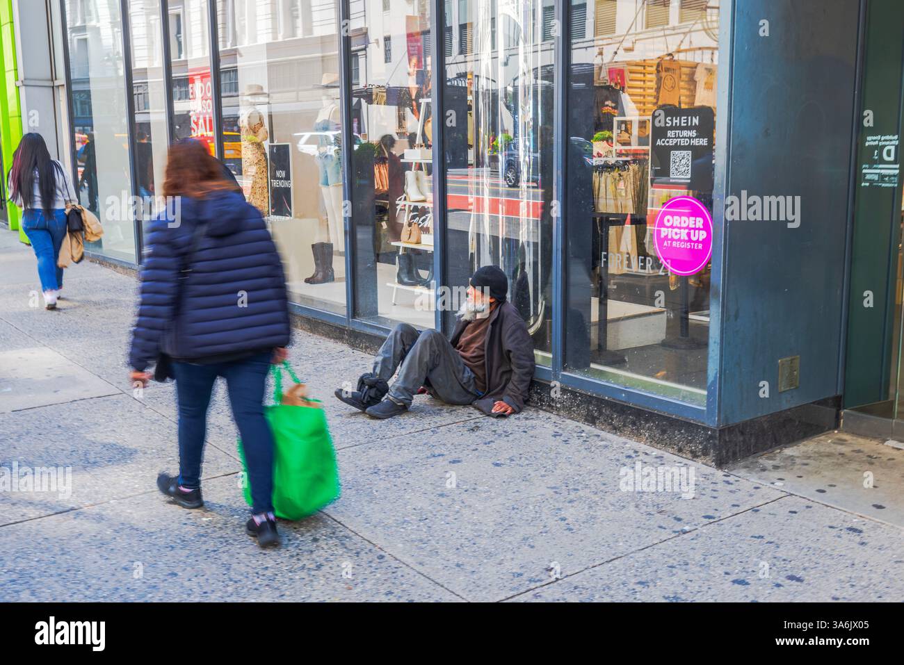 Homme sans-abri assis sur le trottoir près de la fenêtre du magasin tandis que les piétons passent sur la rue animée de la ville. New York. ÉTATS-UNIS. Banque D'Images