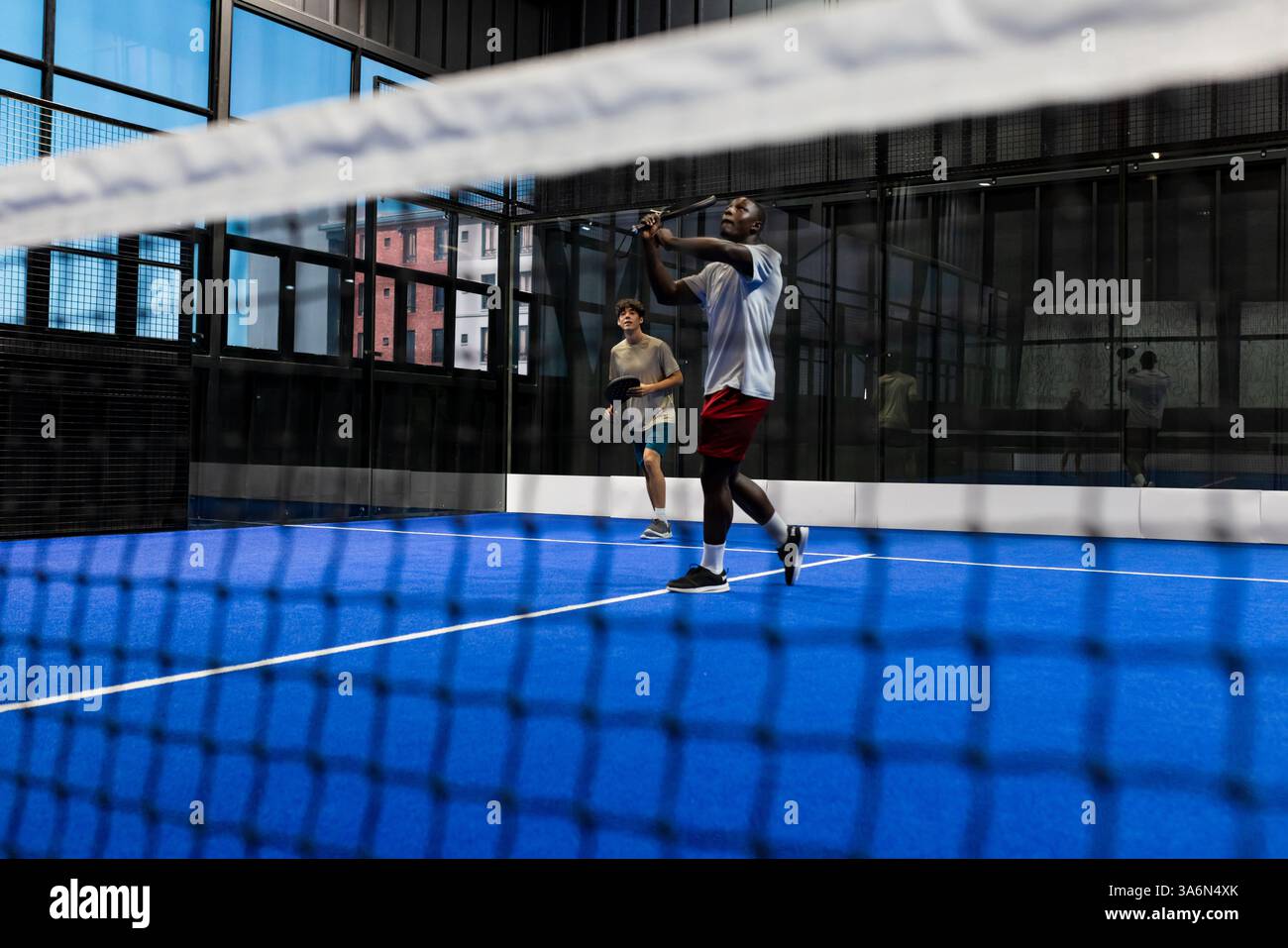 Jouant au padel tennis, deux hommes se concentrant sur frapper la balle dans un court intérieur Banque D'Images