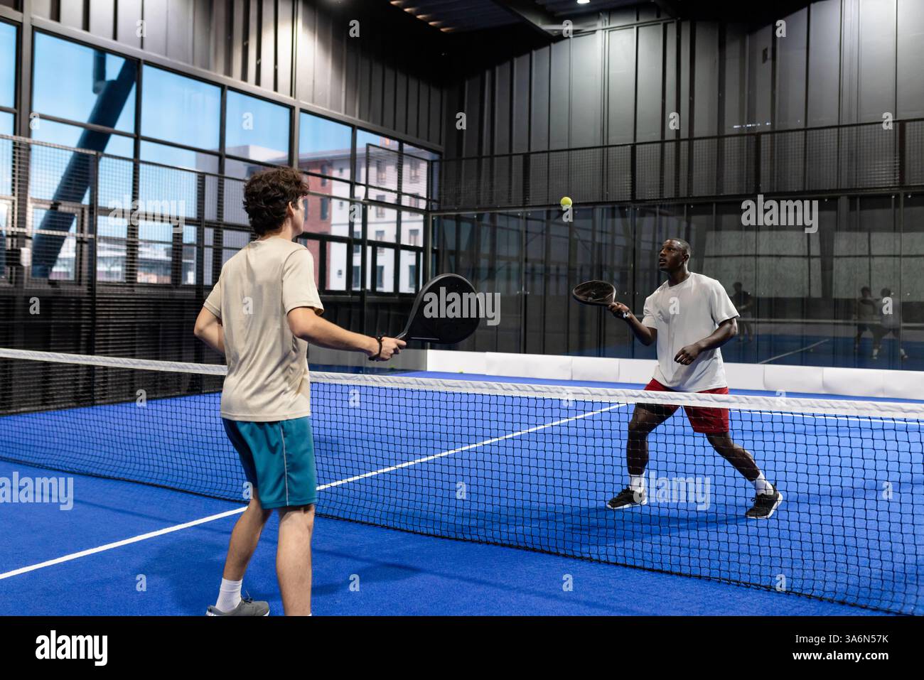 Deux hommes jouant au padel sur un court couvert, en se concentrant sur la balle Banque D'Images