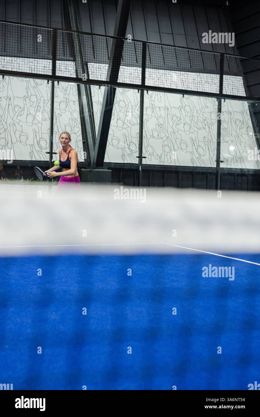 Femme jouant au padel sur un court bleu, souriant et tenant une raquette Banque D'Images
