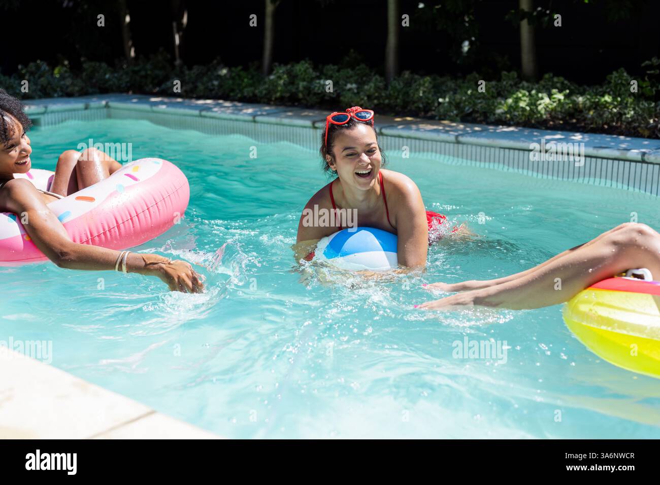 Femmes appréciant la fête de la piscine avec des flotteurs colorés et ballon de plage, riant ensemble Banque D'Images