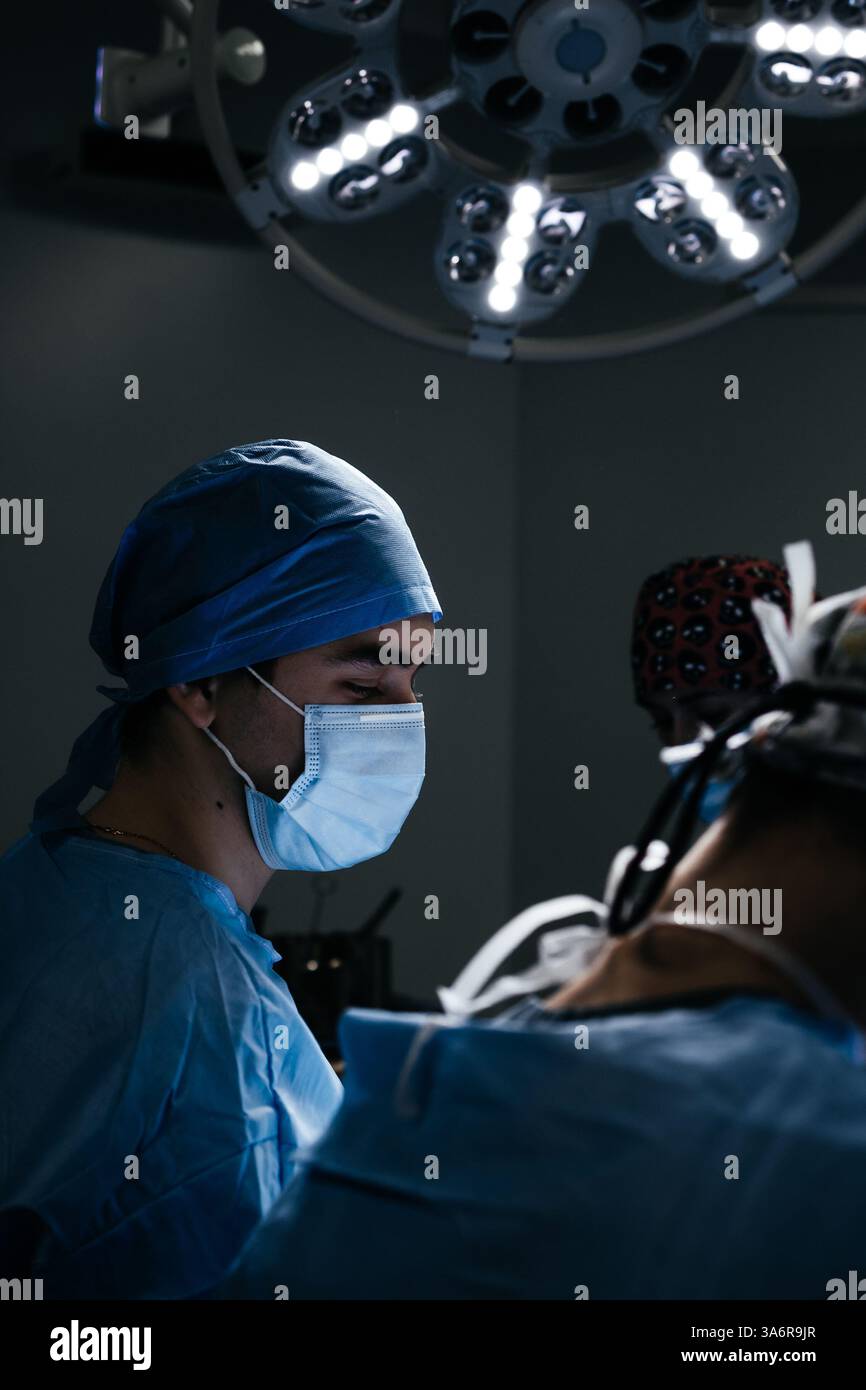 Portrait d'un médecin masculin en masque dans une chambre d'hôpital sombre avec équipement technologique. Chirurgien asiatique a fait de la chirurgie orthopédique ou esthétique. Vertical Banque D'Images