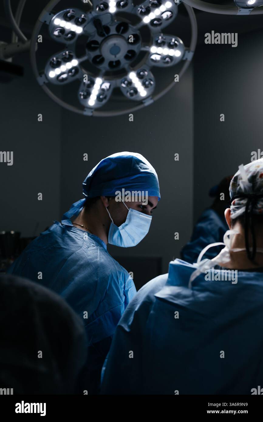 Portrait d'un médecin masculin en masque dans une chambre d'hôpital sombre avec équipement technologique. le chirurgien regarde le moniteur et opère le patient. Prise de vue verticale Banque D'Images