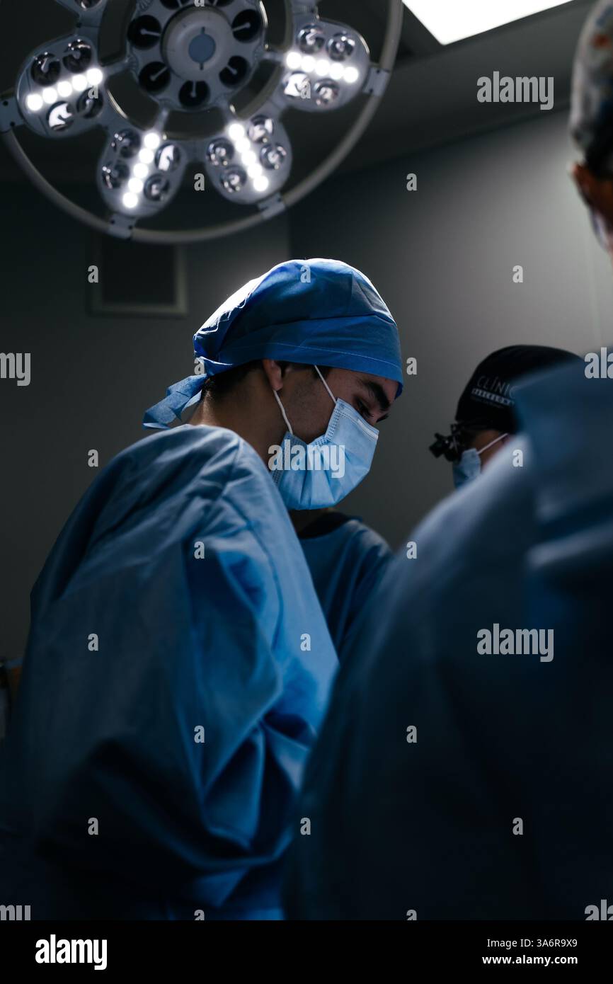 Portrait d'un médecin masculin en masque dans une chambre d'hôpital sombre avec équipement technologique. Chirurgien asiatique a fait de la chirurgie orthopédique ou esthétique. Vertical Banque D'Images