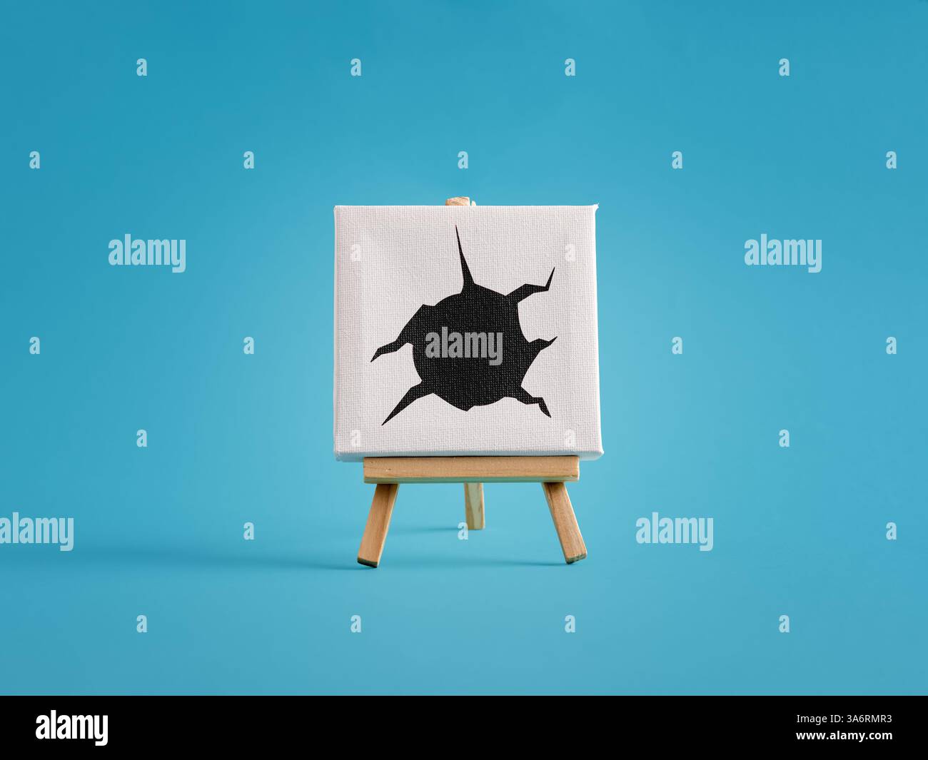 Poartraying dommages, destruction , crime et violation. Le trou de balle noire s'étend du centre d'une toile blanche sur un chevalet en bois contre un blu Banque D'Images
