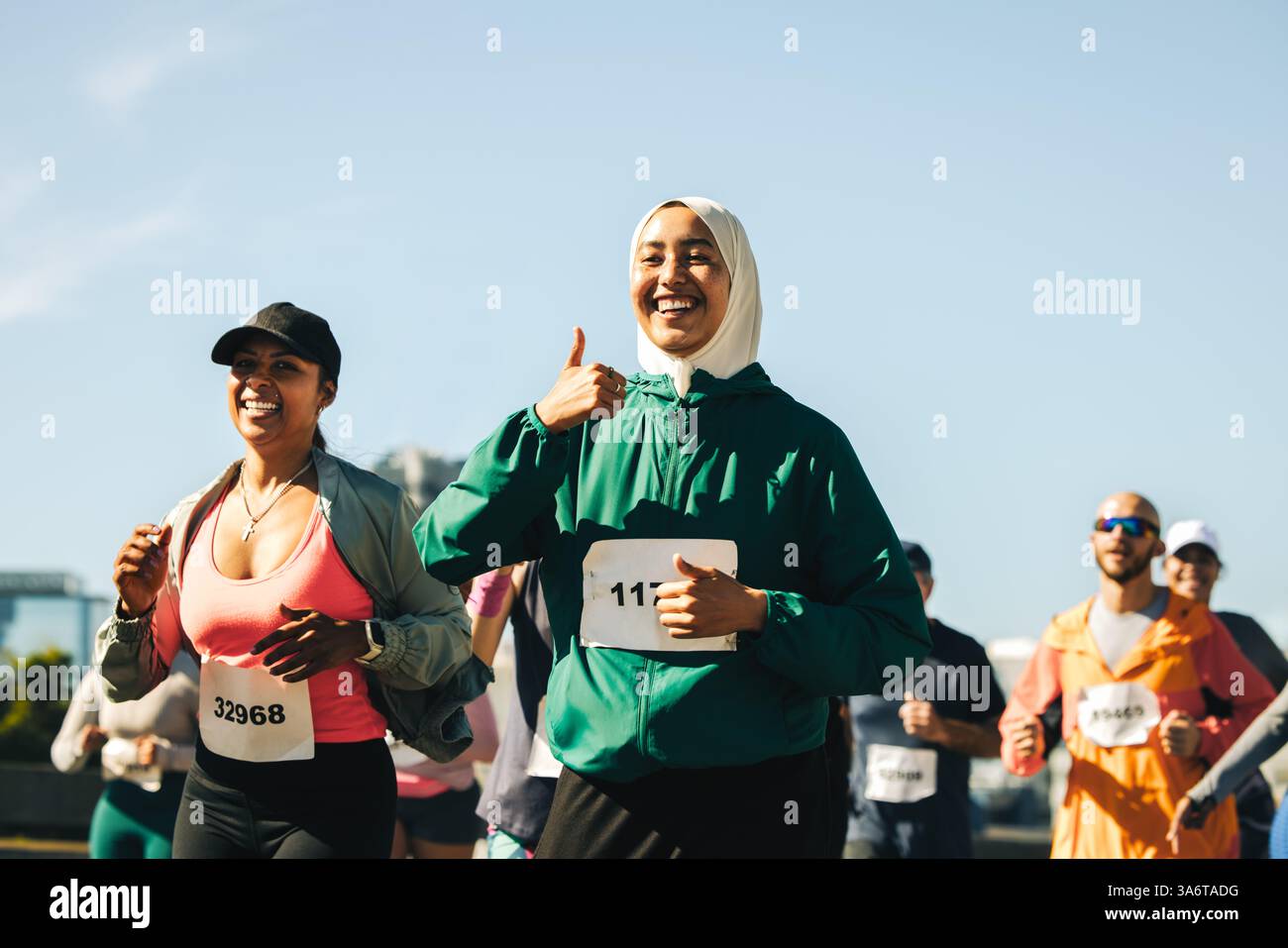 Deux femmes, dont l'une porte un hijab, expriment joie et encouragement alors qu'elles courent une course ensemble, toutes deux donnant le geste pouce levé. La scène capture leur Banque D'Images