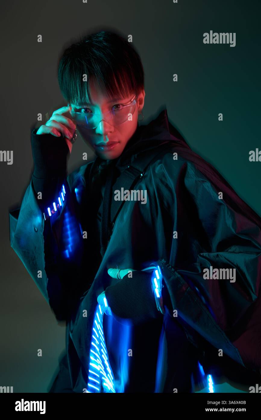 Un homme asiatique élégant arbore une tenue unique avec des éléments lumineux, rayonnant de confiance. Banque D'Images