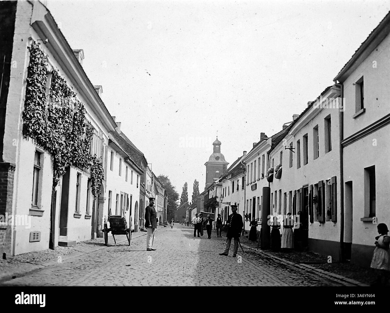 Une scène de rue résidentielle à Linn, un quartier historique de la ville de Krefeld, situé dans l'état de Rhénanie du Nord-Westphalie, Allemagne. Cette photo montre deux gendarmes (policiers) debout sur la route. Les habitants sont sur le trottoir et un chariot à main est à proximité. D’après une collection de photographies d’une tournée européenne familiale qui s’est déroulée en 1899. Les photographies originales étaient d'environ 3 ½ x 2 ½ pouces. Banque D'Images