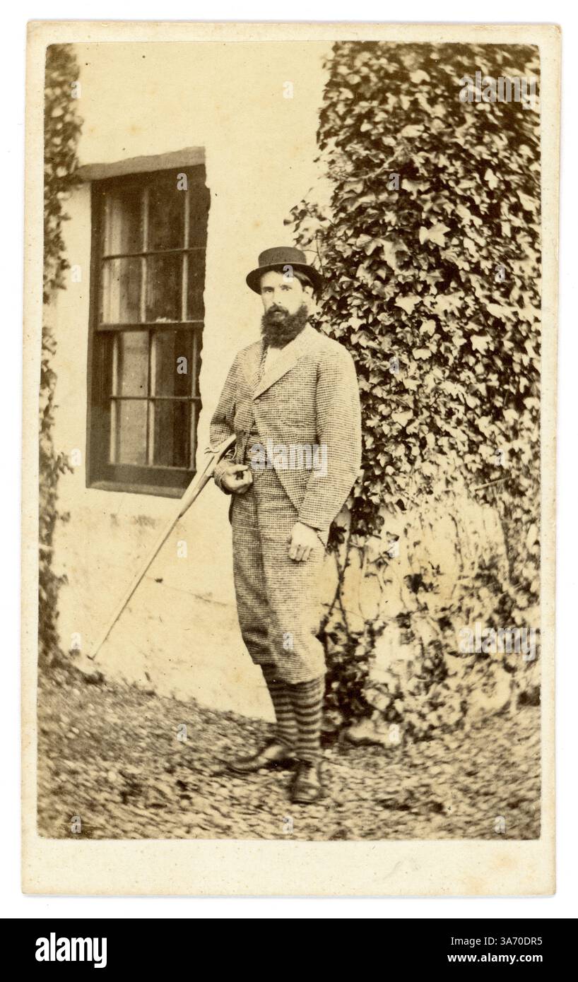 Carte de visite victorienne originale (carte de visite ou CDV) d'un jeune homme victorien barbu attrayant, gentleman victorien, appelé M. John Bateson, portant des vêtements de sport de pays de noblesse débarqué, posant pour une photographie devant sa maison, tenant un fusil de chasse. D'après une collection de la famille Arkwright, Hampton court Castle Hereford, photographié par Marcus Ward & Co 13 Donegall place, Belfast c1867 Banque D'Images
