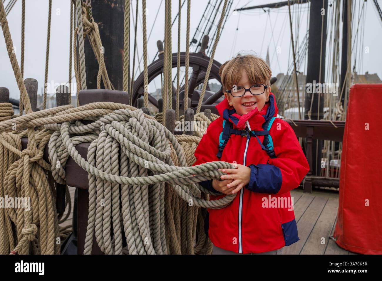 Enfant en manteau rouge sur le bateau, souriant et tenant la corde pendant la visite Banque D'Images